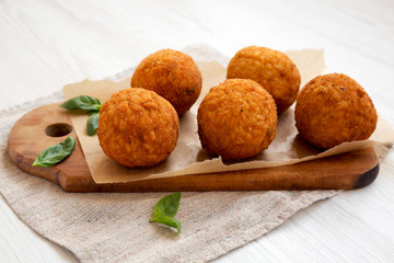 Homemade fried Arancini with basil on a white wooden surface, side view. Italian rice balls. Close-up.