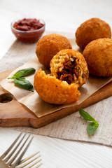 Homemade fried Arancini with basil and Marinara on a white wooden background, side view. Italian rice balls. Close-up.