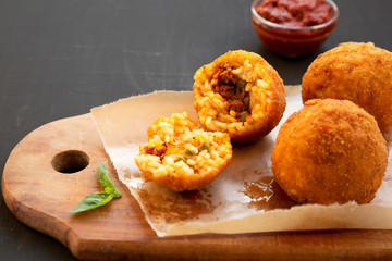 Homemade fried Arancini with basil and Marinara sauce on a black background, side view. Italian rice balls. Copy space.