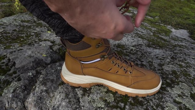 Close up shot of hiking man hands tying shoelaces on leather mountaineering boots standing on mountain peak stock video