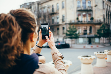 Woman in a beige coat photographs the old city