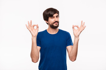Handsome brunet bearded man with mustaches in a blue shirt showing gesture of OK sign with two hands standing isolated over white background.