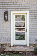 cape cod style home with white wood door at back entrance. Door has many glass windows and outside is an exterior light