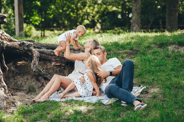 Parents and kids having fun rest outdoors on green meadow.