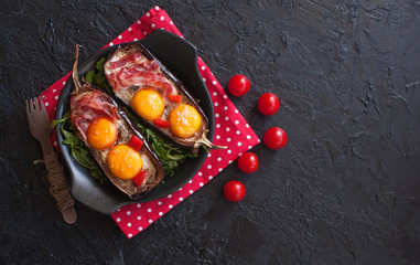 Baked eggplant stuffed with eggs and bacon on a black plate on a black wooden table. Breakfast idea. The view from the top. Copy space