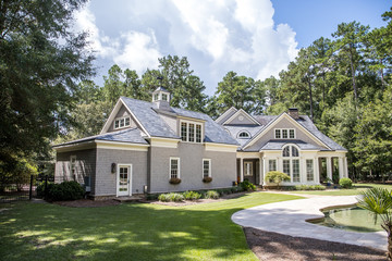 Rear view and backyard of large cape cod style home with columns and windows and a round porch patio