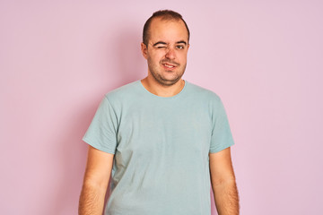 Young man wearing blue casual t-shirt standing over isolated pink background winking looking at the camera with sexy expression, cheerful and happy face.