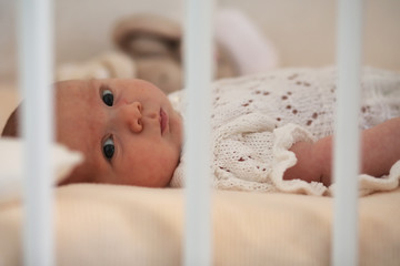 Newborn cute baby lies in the crib and looking mother