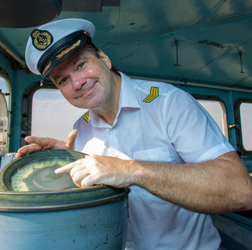 Navigation officer manages devices on the navigation bridge. The captain in the white uniform shows the course of the ship in the wheelhouse.