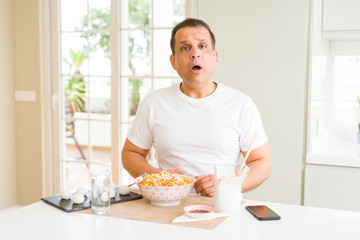 Middle age man eating asian food with chopsticks at home afraid and shocked with surprise expression, fear and excited face.