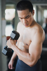 Fototapeta na wymiar Young Asian man exercising with dumbbells and looking at the arm in the gym. Man workout arm at fitness room. Man losing weight training concept.