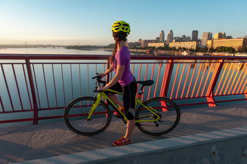 Female bicyclist enjoying beautiful panoramic city view from bridge with red fence