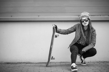 A young hipster girl is riding a skateboard. Girls girlfriends for a walk in the city with a skateboard. Spring sports on the street with a skateboard.