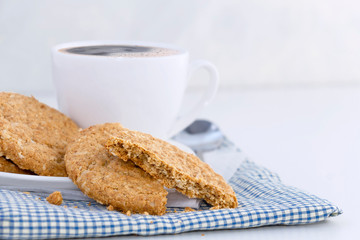 Homemade shortbread cookies made of oatmeal are stacked with hot coffee cup on cloth and paper on white table background. Concept food healthy snack for enjoy in holiday.