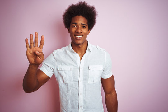 Young american man with afro hair wearing white shirt standing over isolated pink background showing and pointing up with fingers number four while smiling confident and happy.
