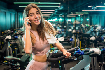 Smiling young woman using phone after cycling training in a spin studio