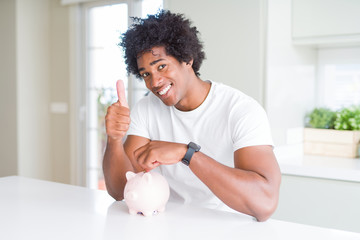 African American man putting a coin inside piggy bank happy with big smile doing ok sign, thumb up...