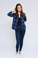 Full-length Vertical Portrait of a cute brunette girl, a young woman with beautiful curly hair in a blue shirt and jeans on a white background. Smiling, talking with emotions, showing hands.