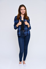 Full-length Vertical Portrait of a cute brunette girl, a young woman with beautiful curly hair in a blue shirt and jeans on a white background. Smiling, talking with emotions, showing hands.