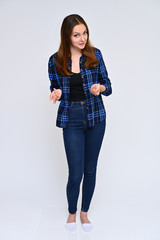 Full-length Vertical Portrait of a cute brunette girl, a young woman with beautiful curly hair in a blue shirt and jeans on a white background. Smiling, talking with emotions, showing hands.