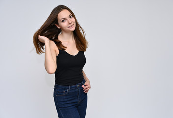 Portrait of a cute brunette girl, a young woman with beautiful curly hair in a black T-shirt on a white background. Smiling, talking with emotions, showing hands to the sides.