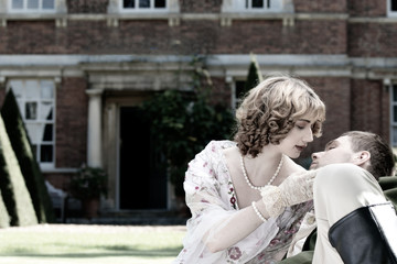 Young couple dressed in vintage costume relaxing and kissing on lawn of stately home