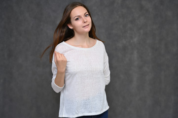 Portrait of a cute brunette girl, a young woman with beautiful curly hair in a white sweater on a gray background. Smiling, talking with emotions, showing hands to the sides.