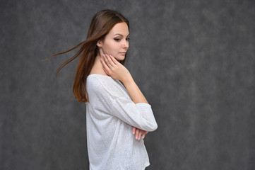 Portrait of a cute brunette girl, a young woman with beautiful curly hair in a white sweater on a gray background. Smiling, talking with emotions, showing hands to the sides.