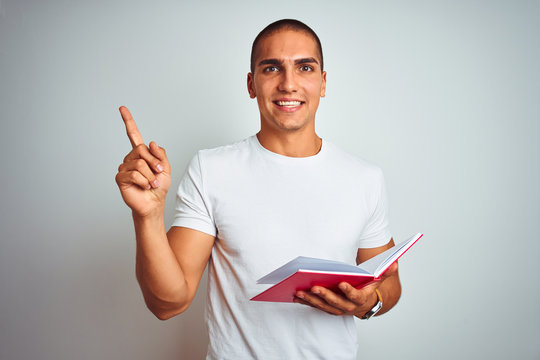 Young handsome man reading red book over white isolated background very happy pointing with hand and finger to the side