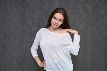Portrait of a cute brunette girl, a young woman with beautiful curly hair in a white sweater on a gray background. Smiling, talking with emotions, showing hands to the sides.