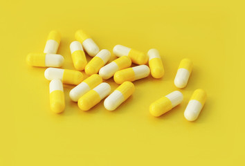 The capsule tablets are half yellow, half white unpacked. Yellow background.