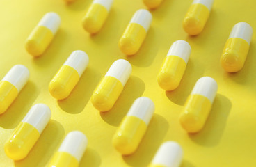 The capsule tablets are half yellow and half white. Arranged in rows. Yellow background.