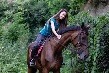 Foto op Canvas Young beautiful brunette girl riding on a horse in the park. © Andrej
