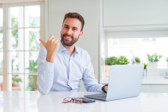 Handsome business man working using computer laptop pointing and showing with thumb up to the side with happy face smiling