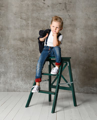 Cute stylish boy sitting on chair near concrete wall