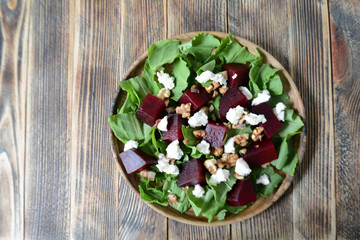 Warm autumn beetroot salad with soft cheese, walnuts and spinach in a plate on a wooden background