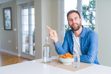 Handsome man eating pasta with meatballs and tomato sauce at home with a big smile on face, pointing with hand and finger to the side looking at the camera.
