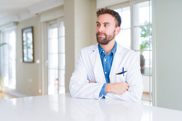 Handsome doctor man wearing medical coat at the clinic smiling looking side and staring away thinking.