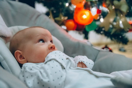 close up on newborn baby looking out, christmas tree in background