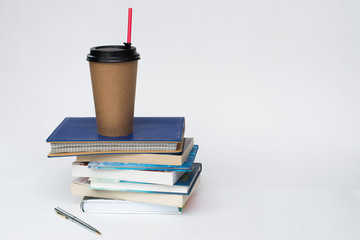 paper Cup for coffee with a red straw stands on a stack of books, white background