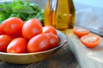 Fresh ripe organic tomatoes in a wooden bowl. Ingredients for summer salad: tomatoes, spinach, olive oil