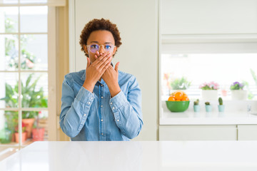 Young beautiful african american woman wearing glasses shocked covering mouth with hands for mistake. Secret concept.