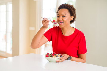 Young beautiful african american woman with afro hair eating healthy wholemeal cereals and berries as healthy breakfast