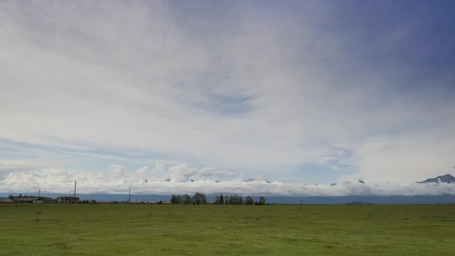 Timelapse. Autumn landscape of a valley with green grass in front of high mountains in cloudy weather with moving clouds on a gray sky