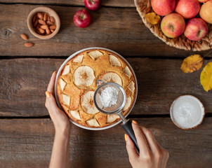 woman's hands with powdered sugar sprinkled on fruit pie on a rustic wooden background, top view
