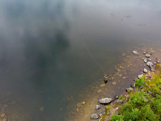 Top view Fisherman man casts rod in mountain river in boots fly fishing salmon, morning. Aerial photo