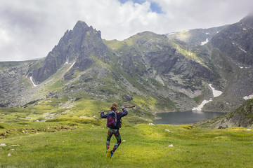 Sporty girl with backpack, tights and hiking stick jumping in front of the Twin glacial lake on Rila mountain and epic pointy summit