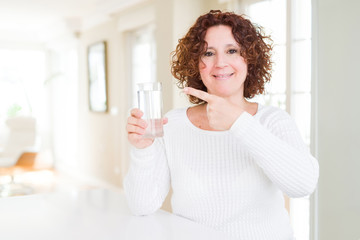 Senior woman driking a fresh glass of water very happy pointing with hand and finger