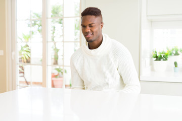 Handsome african american man on white table winking looking at the camera with sexy expression, cheerful and happy face.