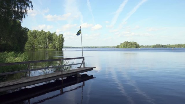 Pan Left to Right: Small Dock with Flag Standing With View of Lake - Smaland, Sweden